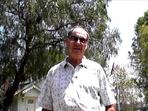 Man in collared shirt and sunglasses in front of a house and trees.