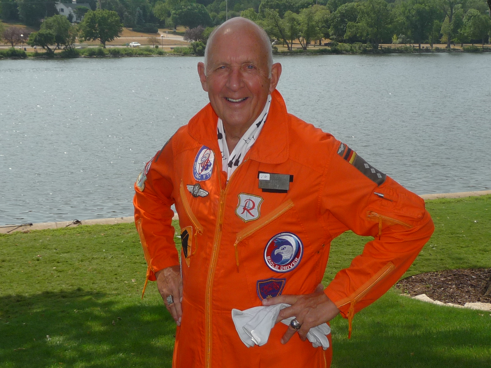 Man standing in front of a body of water in an orange U.S. Air Force utility uniform with patches.  