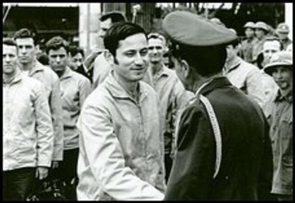 A man shaking an fellow military officers hand in front of a crowd.