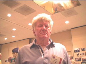 Man in a blue collared shirt with a name card pinned in front of various photographs.