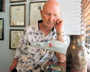 Man gazing at model aircraft and vase with certificates lining the walls. 