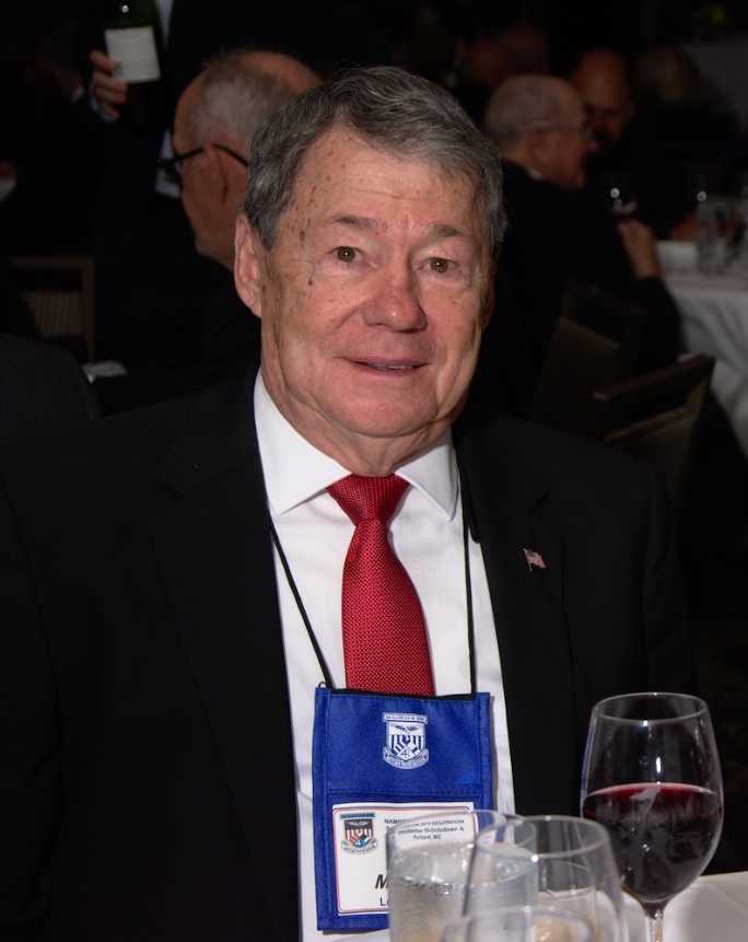 Older man sitting a table in a suit in tie. 