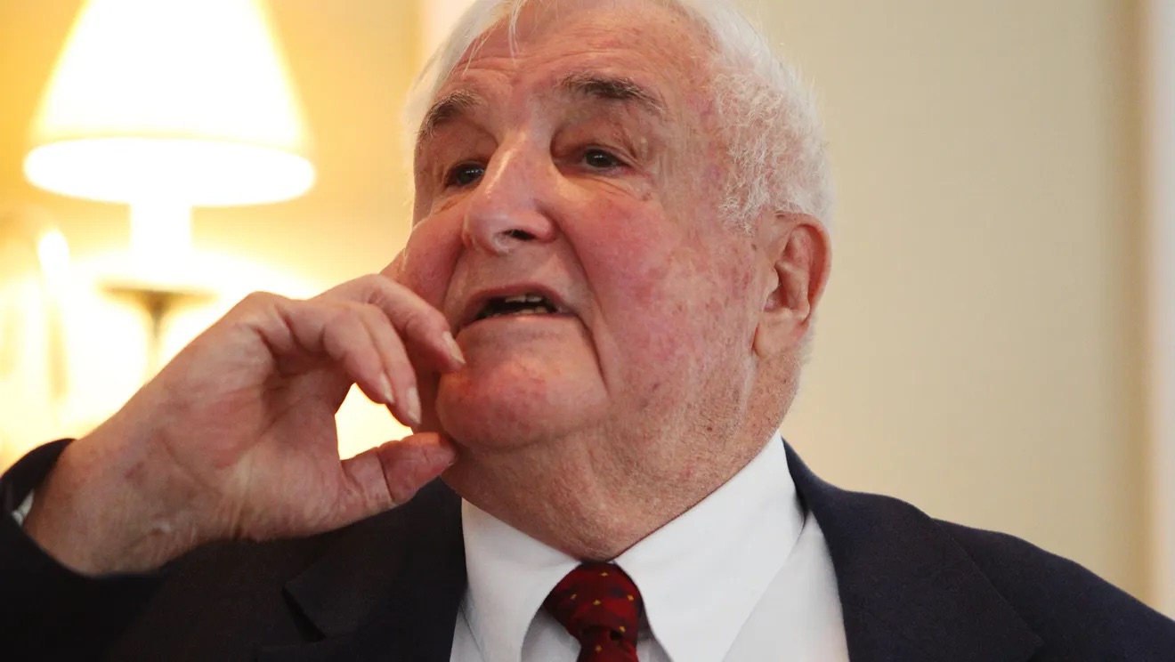 Older man speaking in a suit and tie.