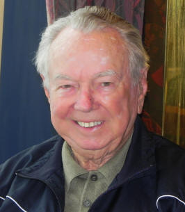 Older man in a green collared shirt and navy jacket.