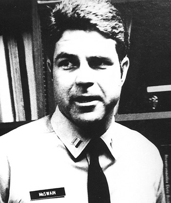 Man in a suit and tie standing in front of a bookshelf.