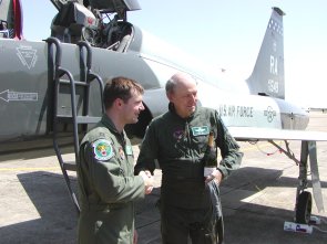 Two men in a U.S. Air Force utility uniforms shaking hands in front of a military aircraft.