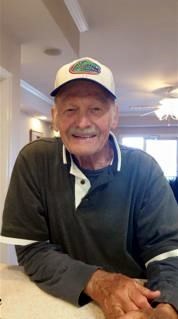 Man smiling in a black and white collared shirt and white hat.