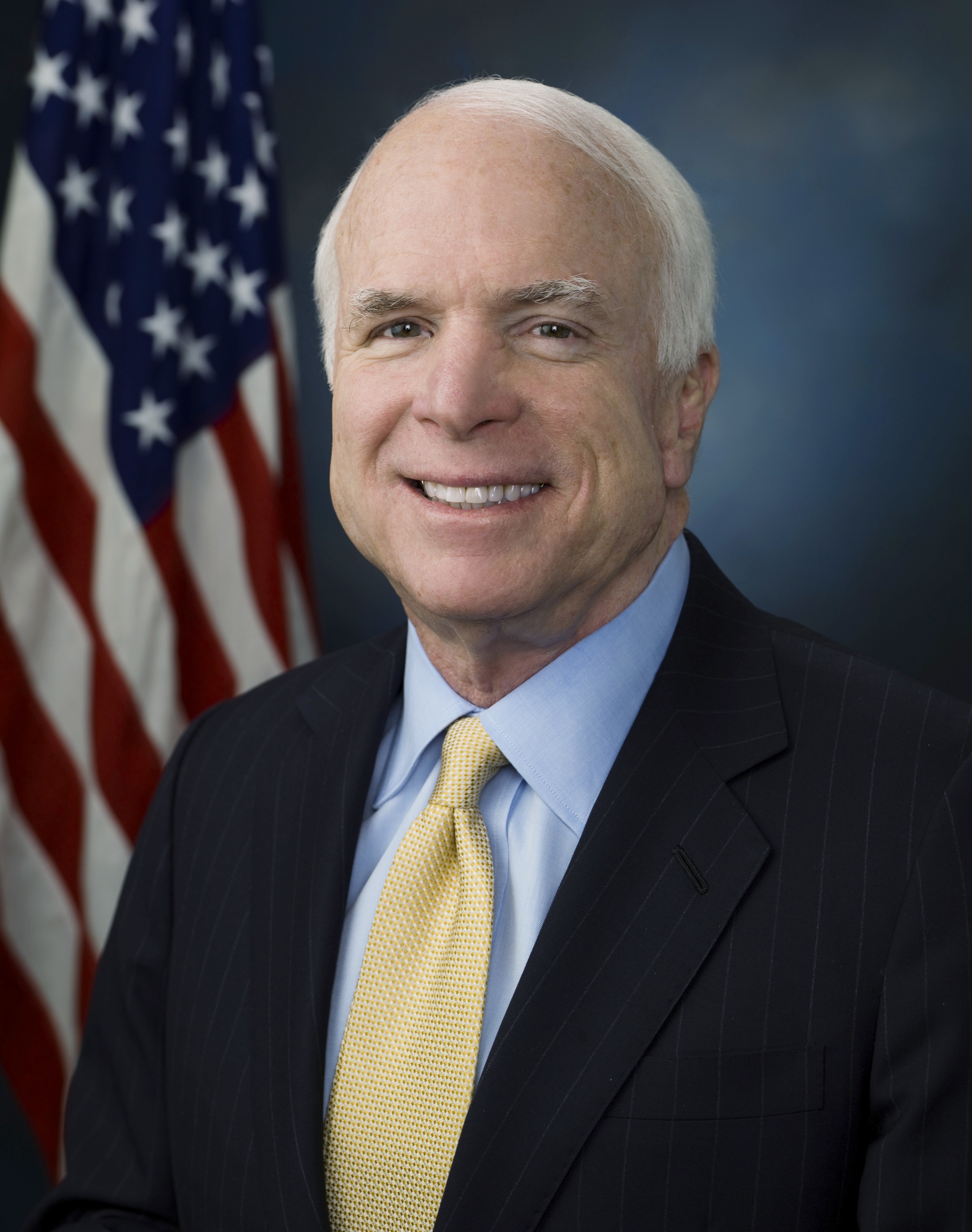 Male in suit in front of American flag.