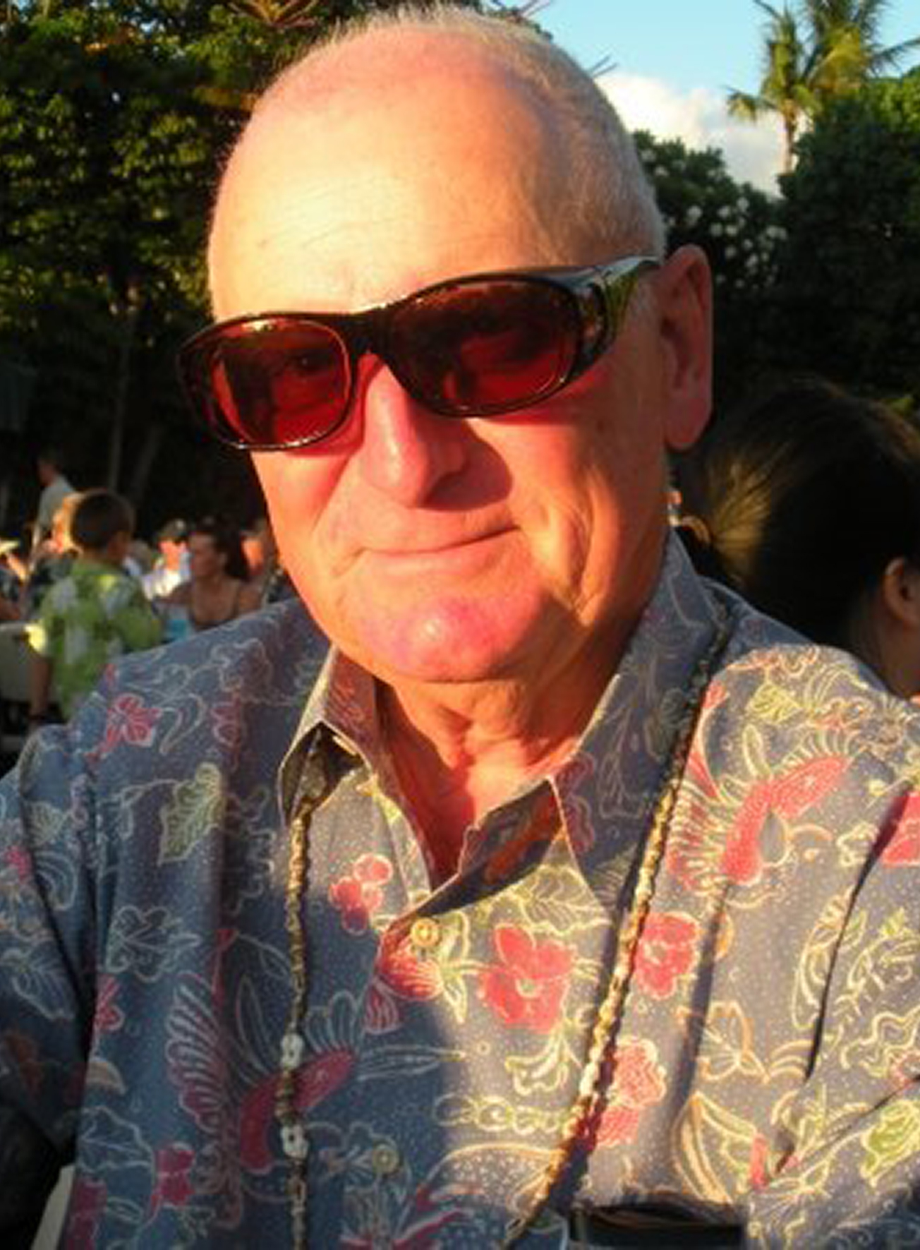 Older man in sunglasses and floral printed collared shirt.