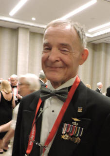 Older man in a suit and bow tie with military pins and a red lanyard.