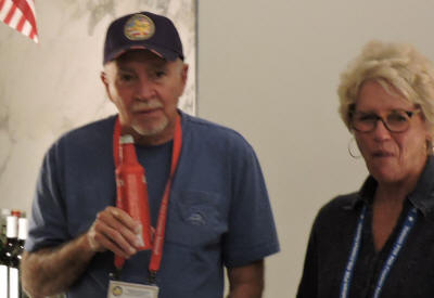 A man in a military baseball cap holding a can next to a woman in glasses.