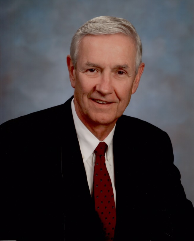 Older man in a black suit and red tie smiling.