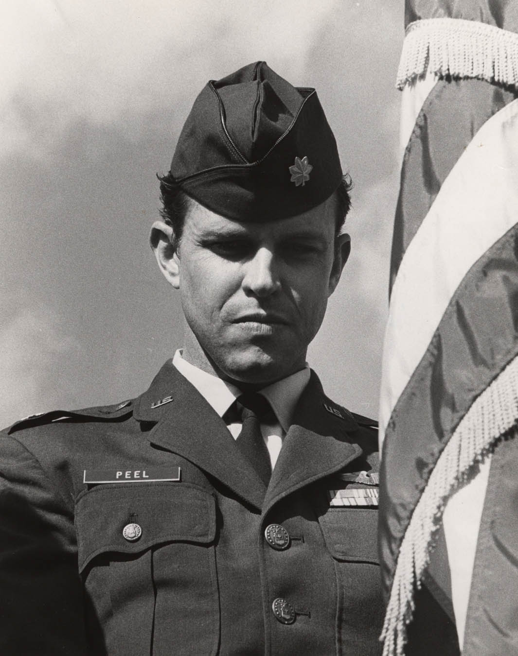 Man in U.S. Air Force suit and cap standing with an American flag.