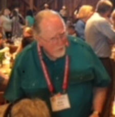 Older man in a green collared shirt in a room full with people.