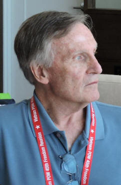 Profile of an older man in a blue collared shirt and red lanyard.