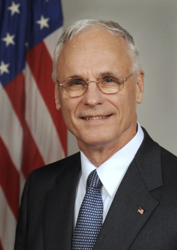 Man in suit sitting in front of American flag.