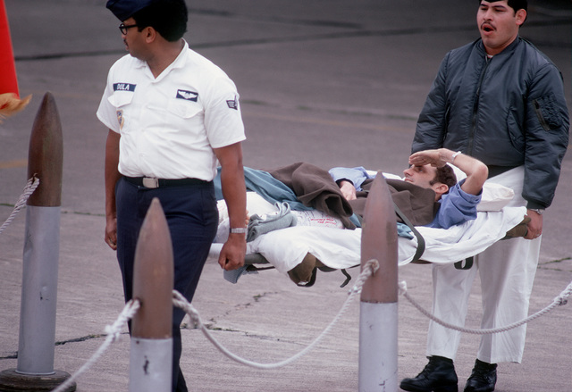 Man saluting from a medical stretcher being carried by two officers.