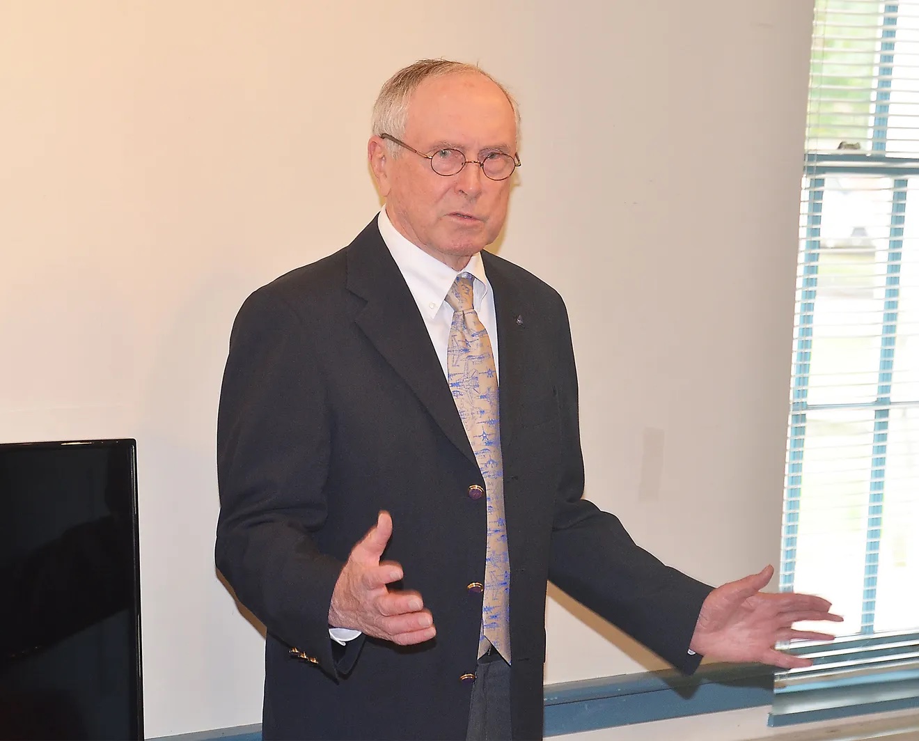 Older man speaking wearing a suit and glasses.