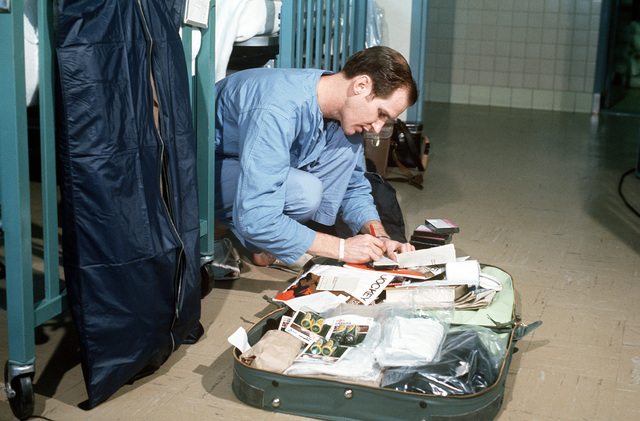 Man wearing blue pants and shirt packing a suitcase in a hospital.