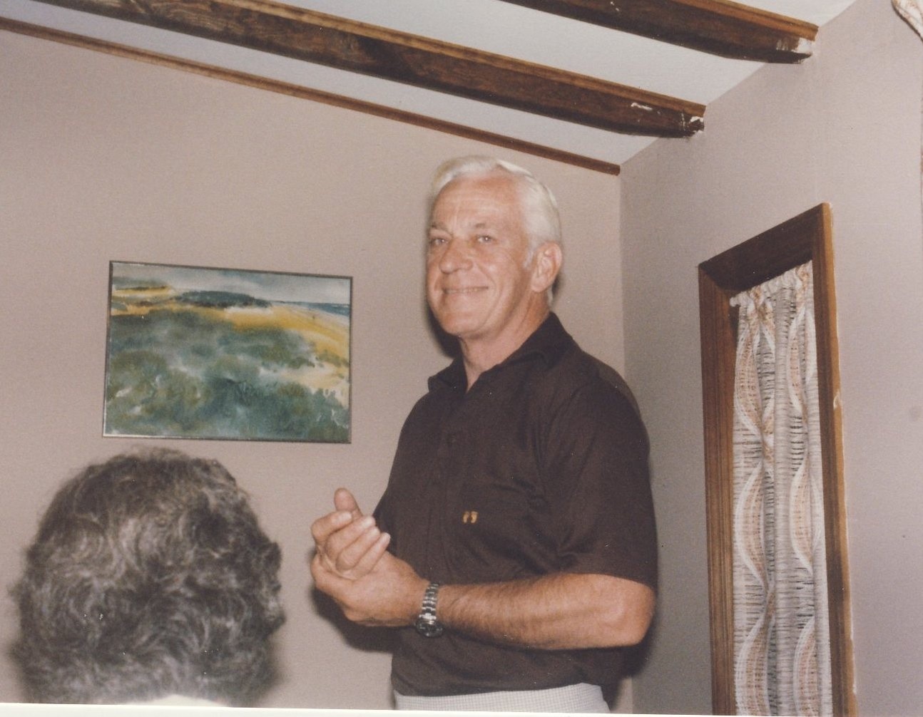 Older man standing in a room smiling in front of a painting.