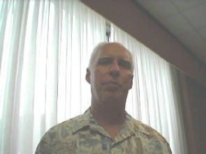 Older man standing in front of a shaded window.