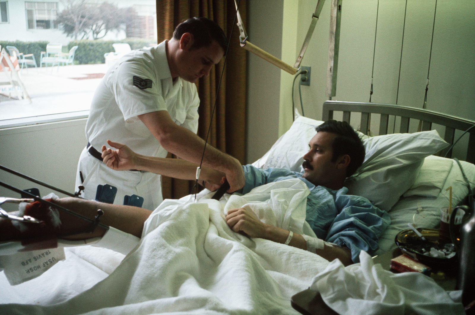 Man in hospital bed being tended to by a doctor.