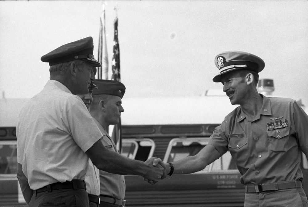 Officers shaking hands in front of a bus and American flags.