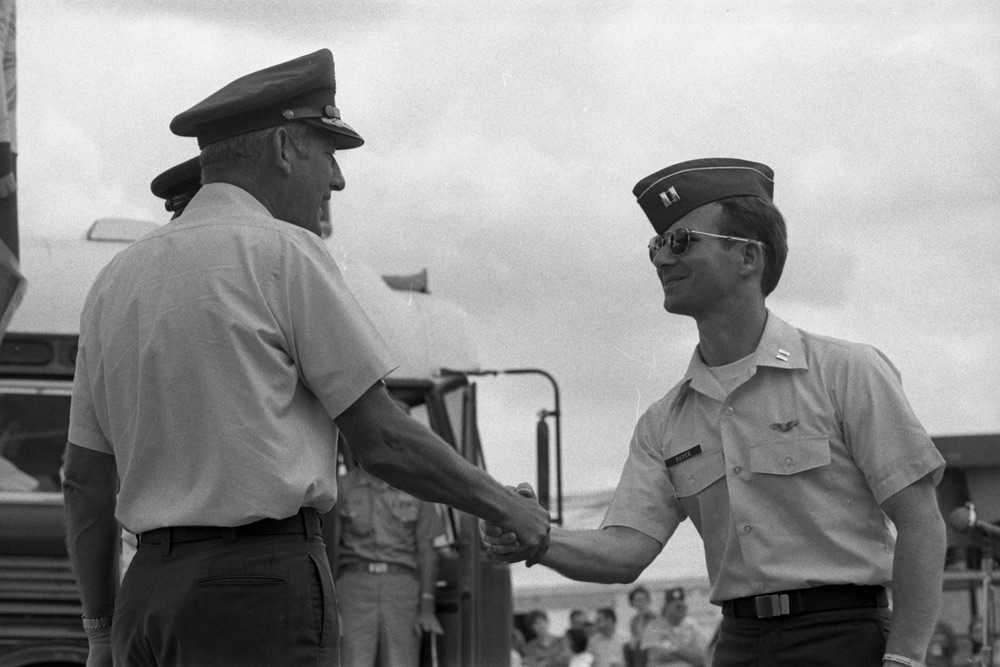 Two officers shaking hand in front of a bus and crowd.