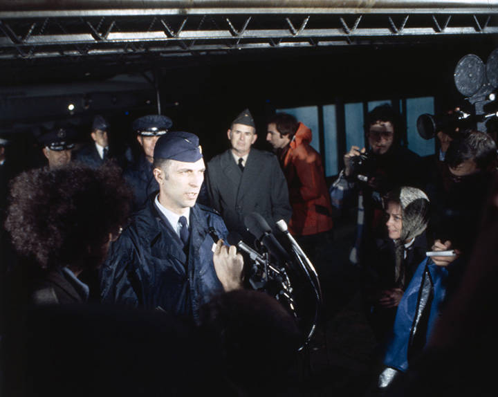 Officer speaking at a microphone in front of fellow officers and reporters.