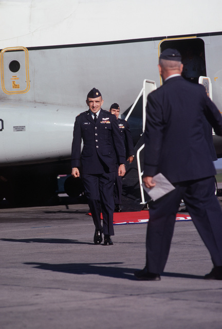 Men in military uniform and cap walking on tarmac in front of military aircraft.