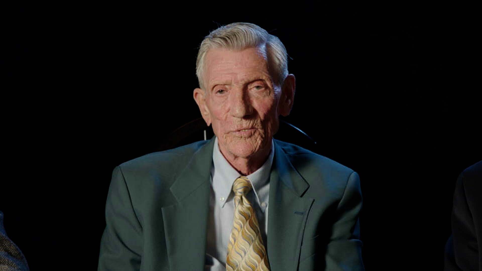 Man on a black screen in a suit and tie.