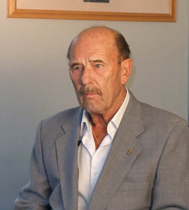 Man sitting in a suit in front of a grey wall.