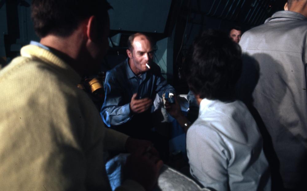 Man smoking a cigarette with a group of people on an aircraft.