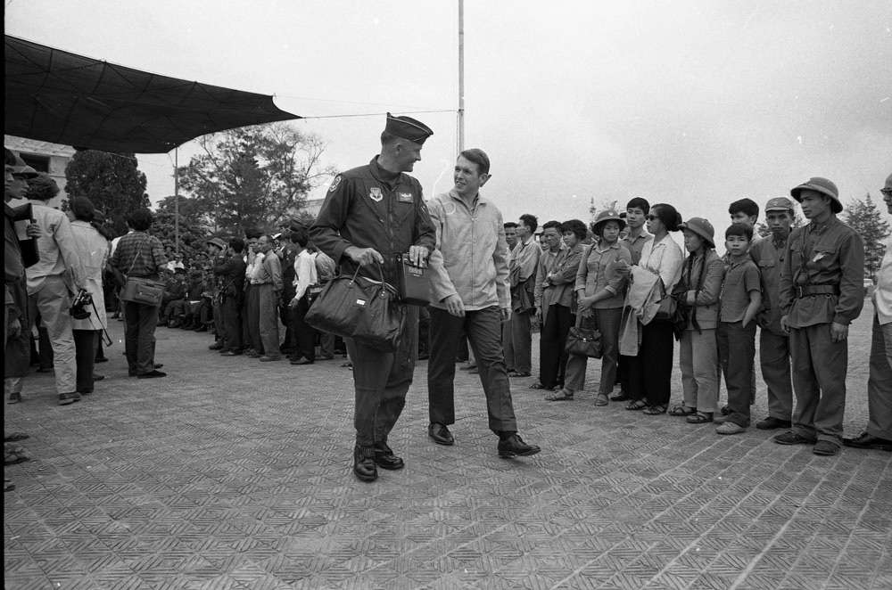 Man walking with an officer in front of a crowd.