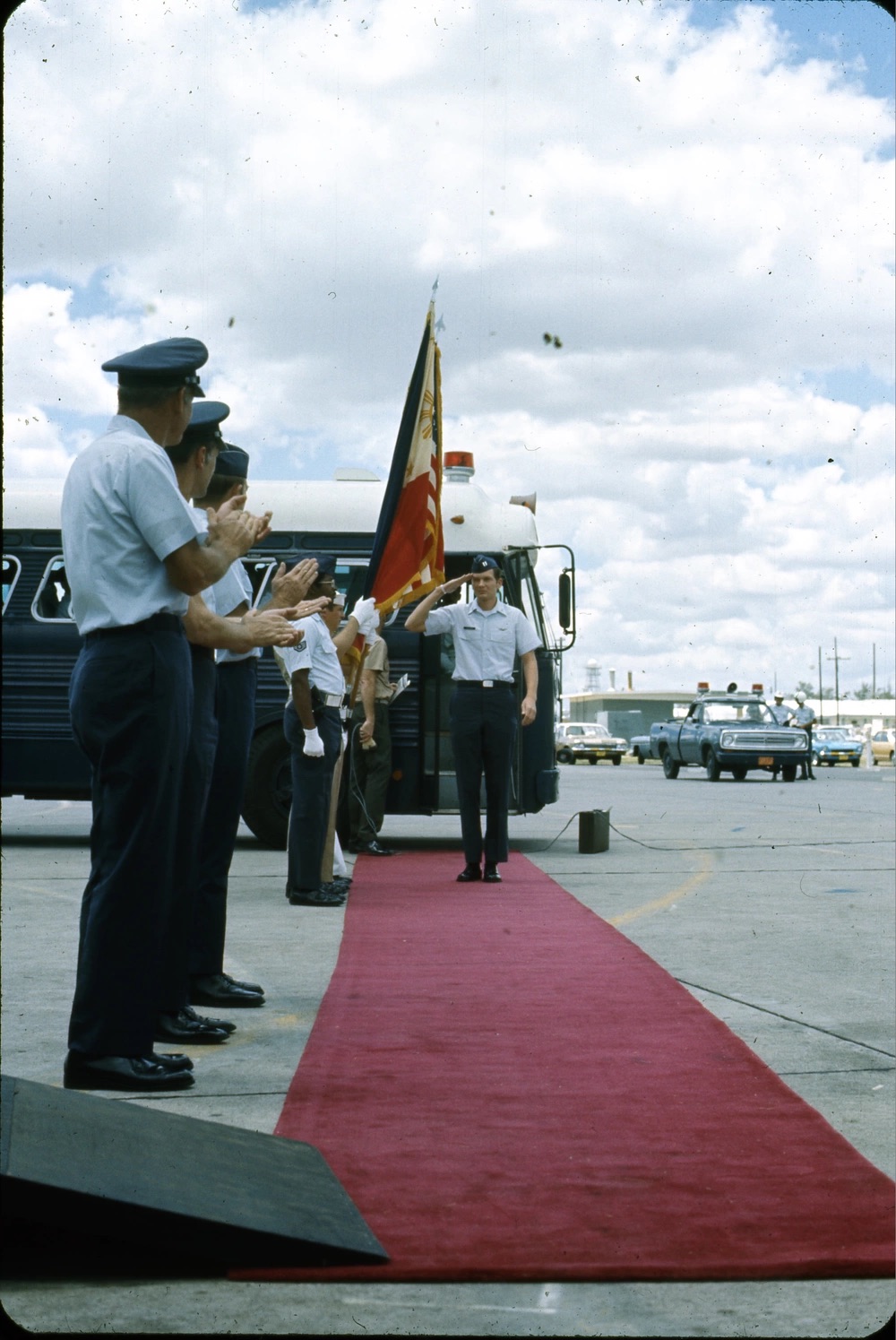 Military officer saluting at the end of a red carpet lined with fellow officers on a tarmac.