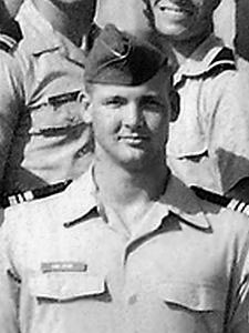 Man in a military uniform standing in a group with fellow officers.