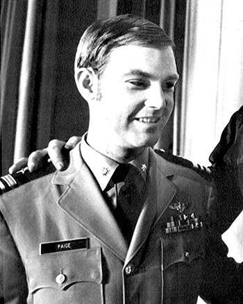 Man in front of curtain in a U.S. Navy uniform.