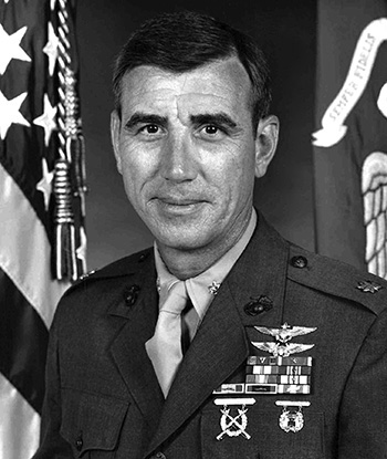 Man in a decorated U.S. military suit in front of an American flag.