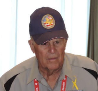 Man in a collared shirt and hat in front of a window.