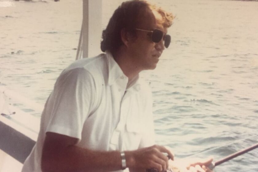 Man on a boat with a white button down shirt and sunglasses fishes off the side of boat.