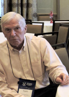 Older man in a collared shirt in a conference room of tables and chairs.