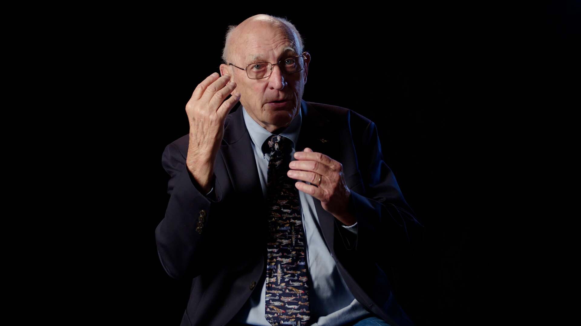 Older man speaking wearing a suit and tie.